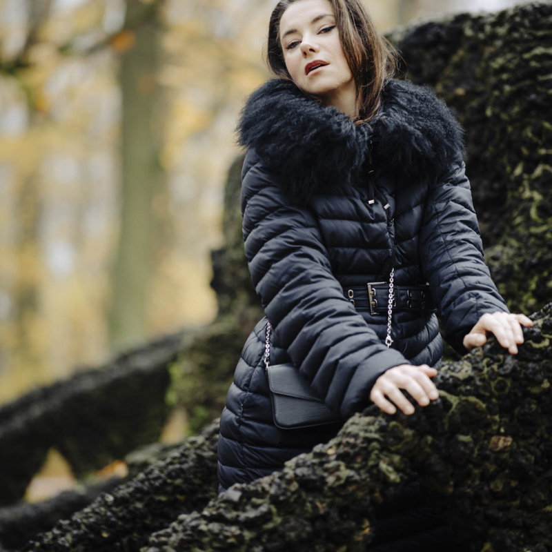 Anna w zimowym stroju, stojąca na kamiennych schodach w toruńskim parku, w nastrojowym świetle popołudnia.