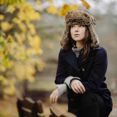 Portret modelki w zimowym płaszczu i czapce-uszatce, sfotografowanej w miękkim, naturalnym świetle na ławce na Barbarce w Toruniu