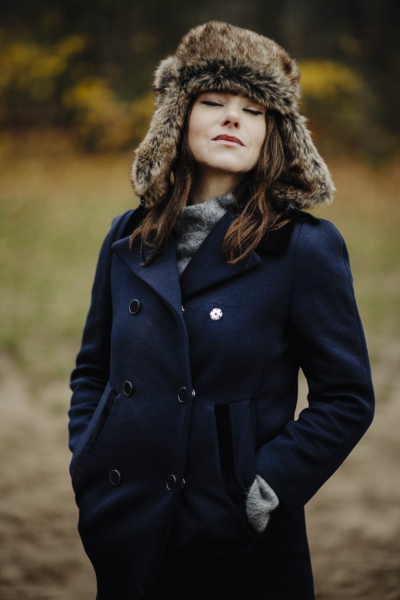 Portret rozmarzonej modelki w płaszczu i futrzanej czapce na tle jesiennej scenerii parku